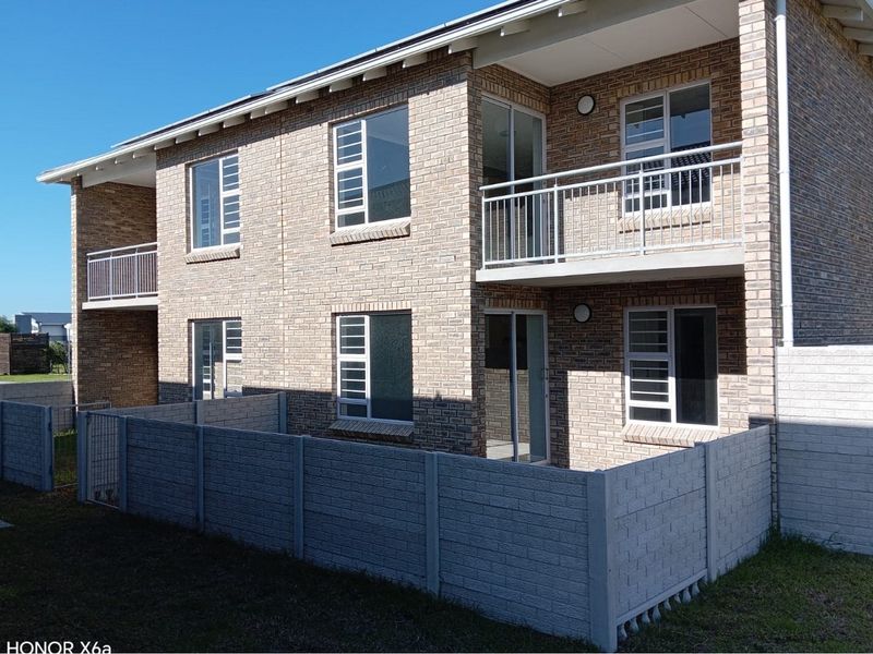 Rear view of a double-storey townhouse featuring face brick construction, upper-level balconies with metal railings, and a private enclosed garden area.