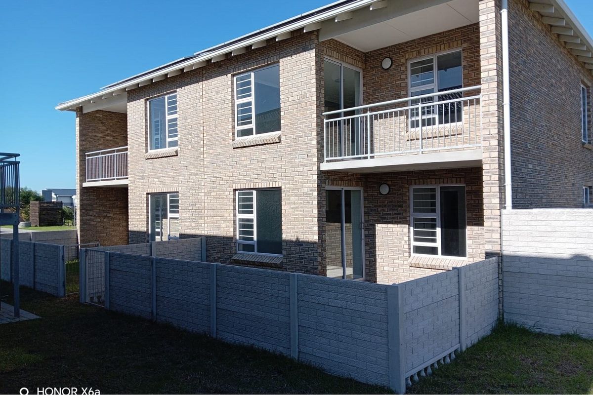 Rear view of a double-storey townhouse featuring face brick construction, upper-level balconies with metal railings, and a private enclosed garden area.