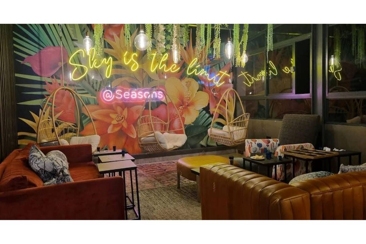 A vibrant, modern lounge area featuring decorative wall murals, neon signage, and contemporary hanging seating, creating a stylish and inviting atmosphere.