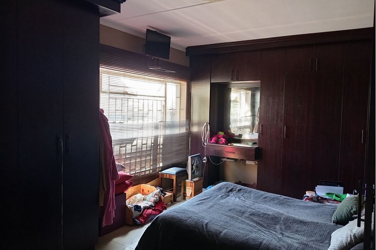 A bedroom featuring extensive dark wood built-in cabinetry and a vanity area, with large windows fitted with horizontal blinds.