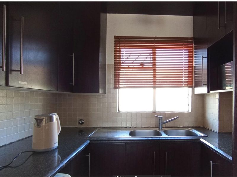 Compact kitchen featuring dark wood cabinetry, granite countertops, a double bowl stainless steel sink, and tiled backsplash.