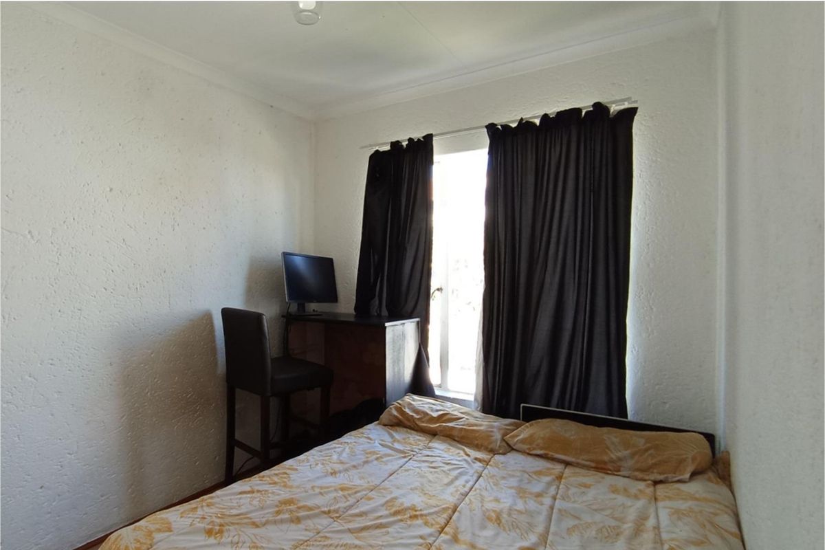 A standard bedroom featuring textured walls, coving, and a window with curtains, providing a functional living space.