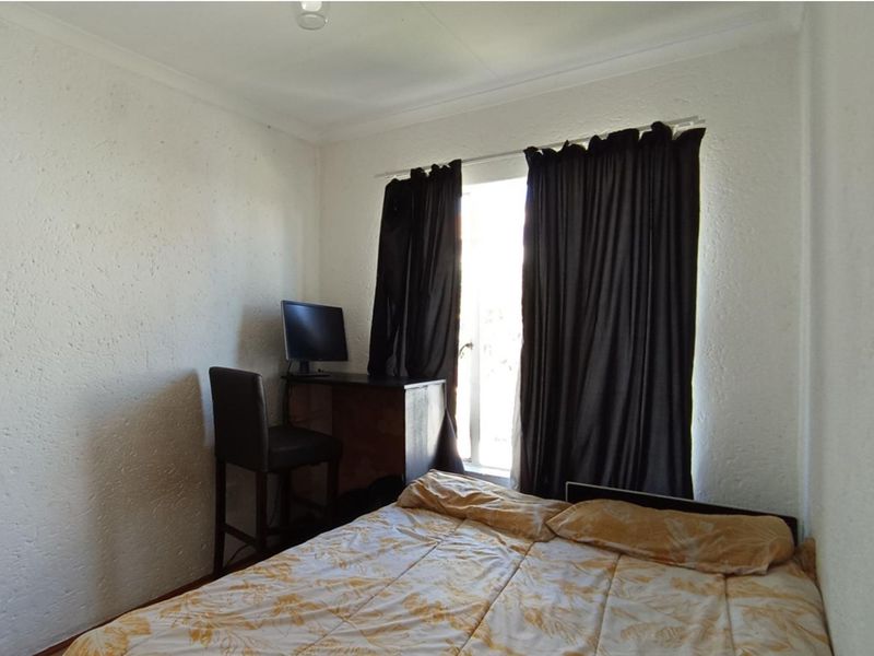 A standard bedroom featuring textured walls, coving, and a window with curtains, providing a functional living space.