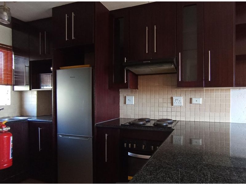 A functional kitchen featuring dark wood cabinetry, granite countertops, a tiled backsplash, and integrated appliances including an electric hob and oven.