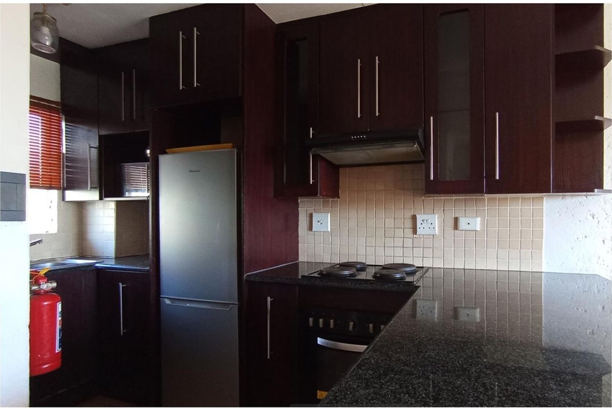 A functional kitchen featuring dark wood cabinetry, granite countertops, a tiled backsplash, and integrated appliances including an electric hob and oven.