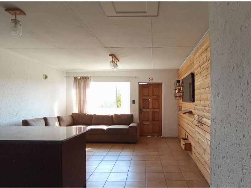 A living area featuring tiled flooring, timber wall cladding, and a solid timber entrance door, offering a rustic aesthetic.