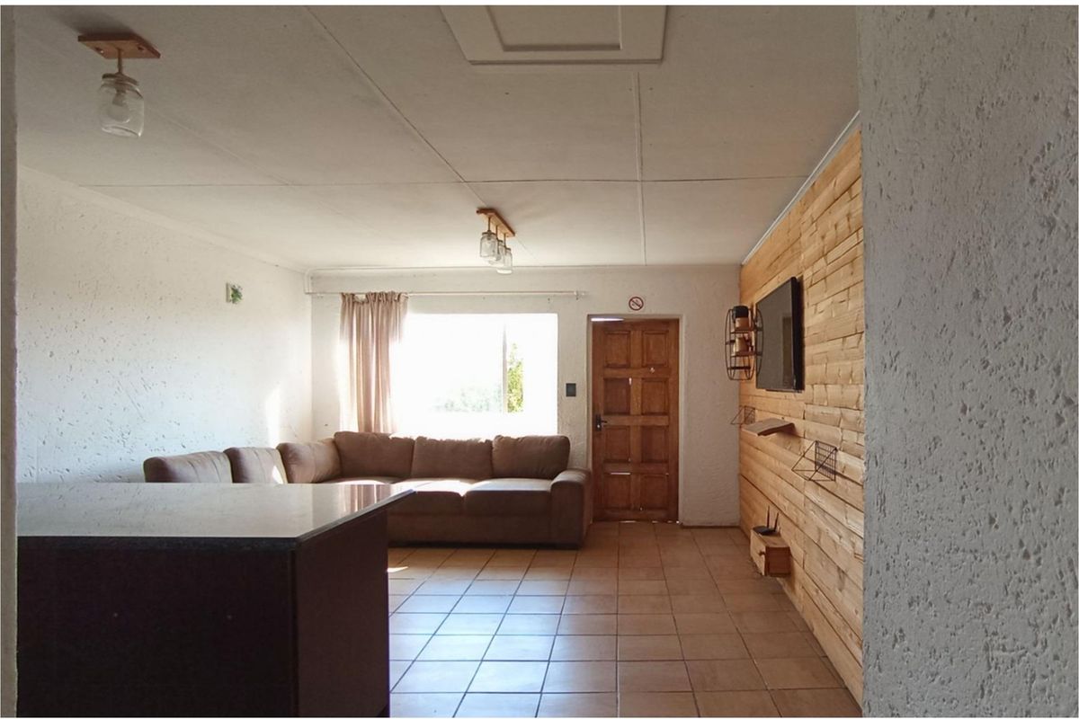 A living area featuring tiled flooring, timber wall cladding, and a solid timber entrance door, offering a rustic aesthetic.