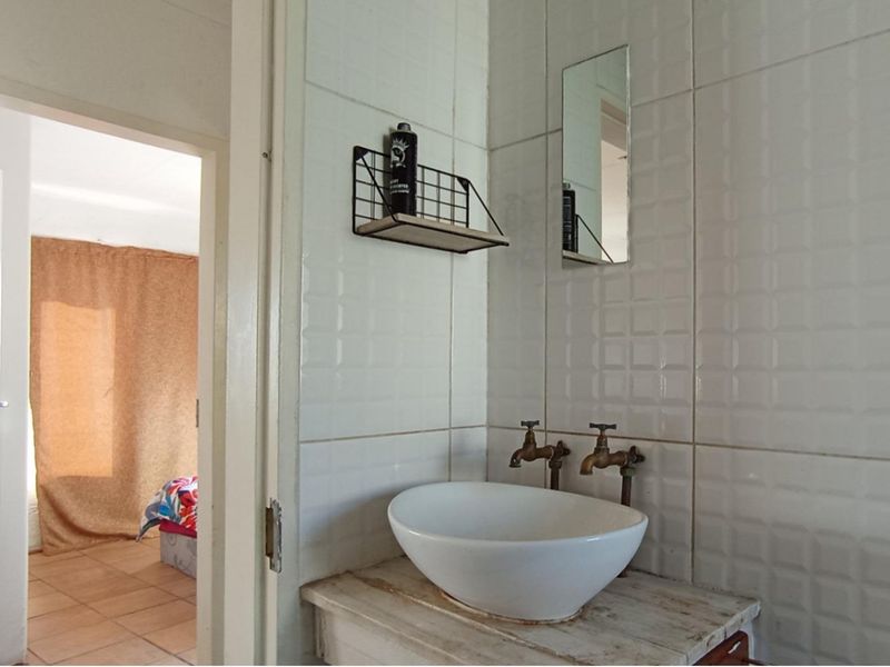 A compact bathroom featuring a vessel sink with wall-mounted taps and tiled walls, showing signs of wear and dated finishes.