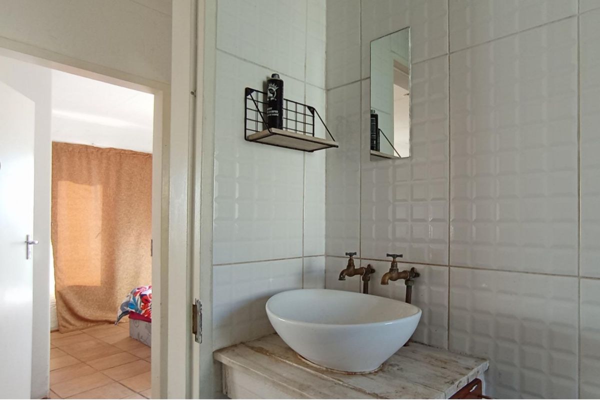 A compact bathroom featuring a vessel sink with wall-mounted taps and tiled walls, showing signs of wear and dated finishes.