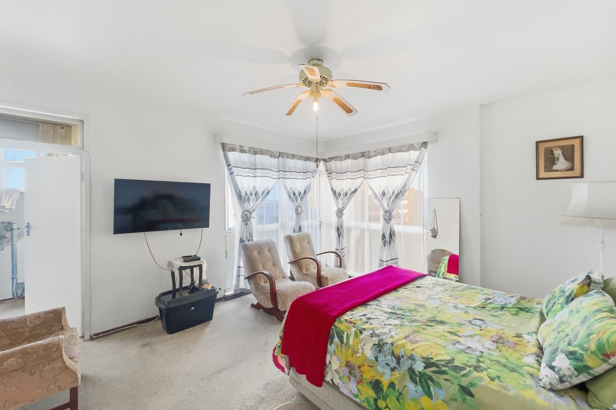 A spacious bedroom featuring a ceiling fan, large windows with natural light, and direct access to an adjoining balcony area.