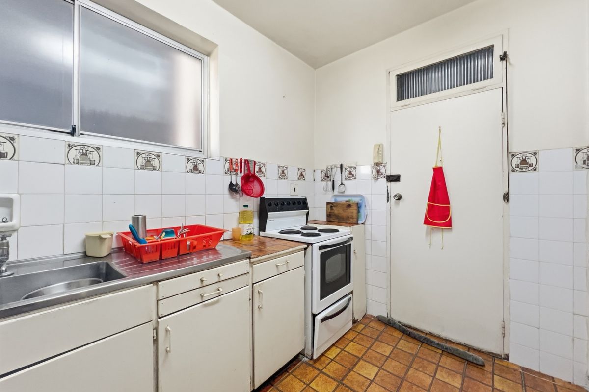 A functional kitchen featuring tiled flooring, built-in cabinetry, a stainless steel sink, and a freestanding stove, with direct access to an exterior door.
