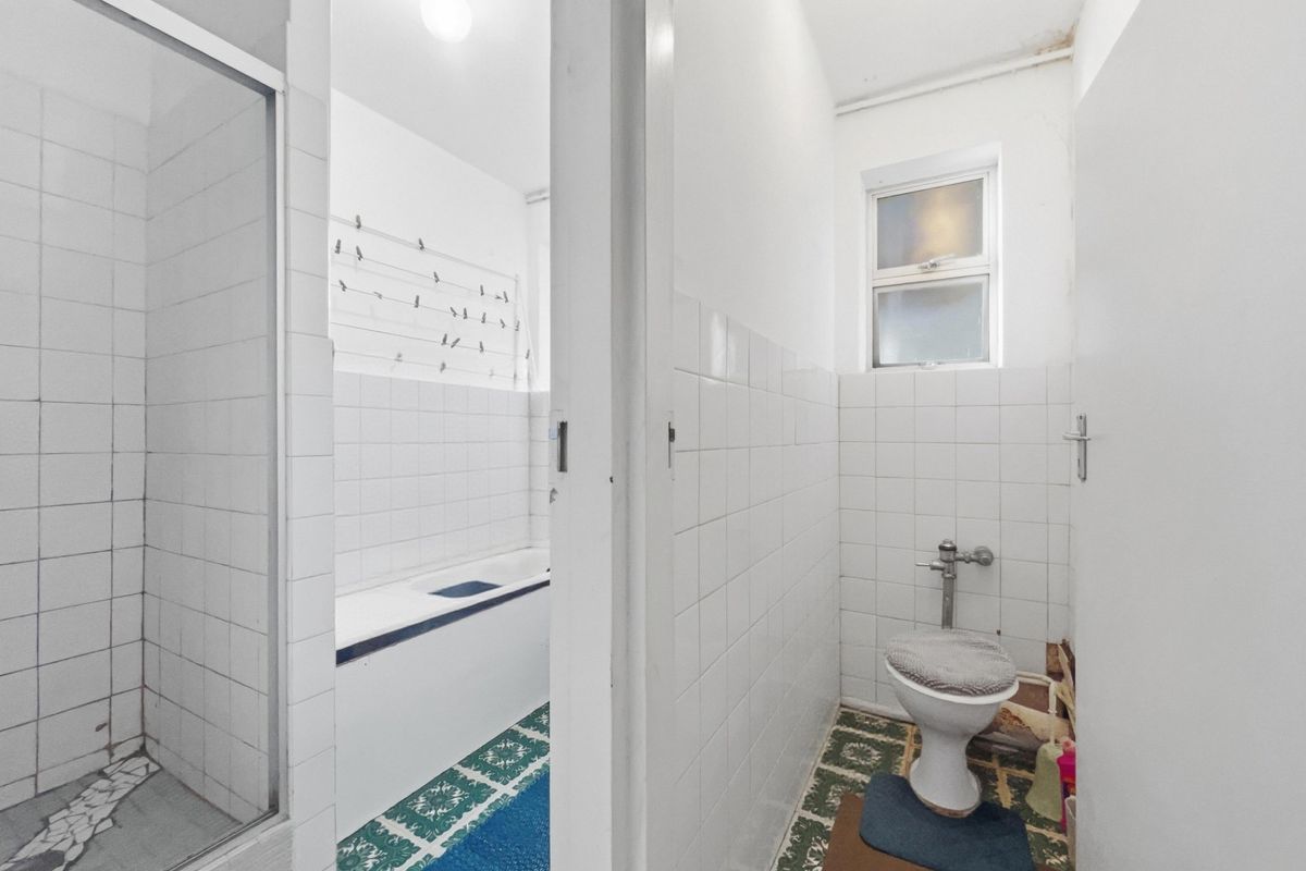 A dated bathroom featuring a separate shower cubicle, bathtub, and toilet with original tiled flooring and wall finishes.