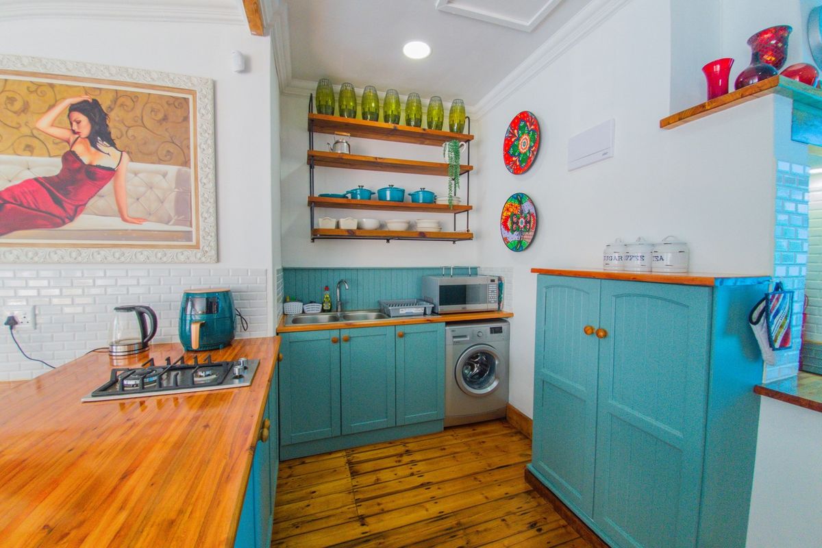 A charming kitchen featuring teal cabinetry, warm timber countertops, subway tile backsplash, and integrated laundry facilities, complemented by natural timber flooring.