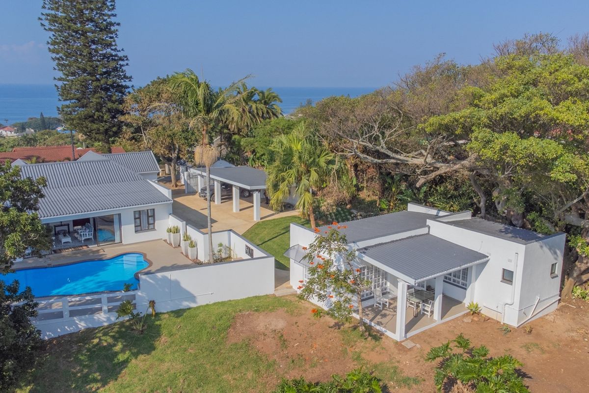 Aerial view of a residential property featuring a swimming pool, covered patio, carport, and well-maintained outdoor spaces with ocean views.