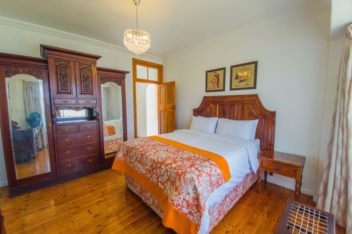 A well-maintained bedroom featuring polished hardwood flooring, crown molding, and a classic crystal chandelier, offering a warm and inviting atmosphere.