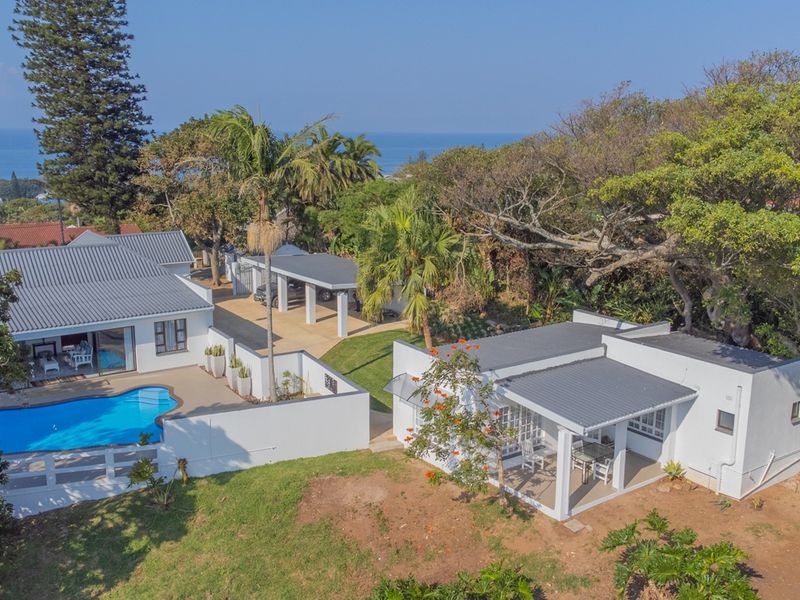 Aerial view of a residential property featuring a swimming pool, covered patio, carport, and well-maintained outdoor spaces with ocean views.