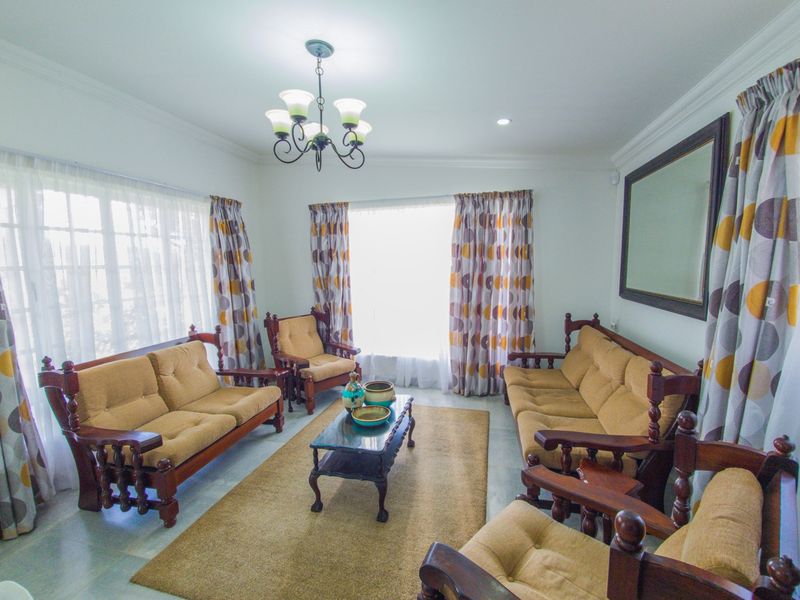 A well-lit living room featuring crown molding, a central chandelier, and tiled flooring, offering a comfortable and traditional living space.