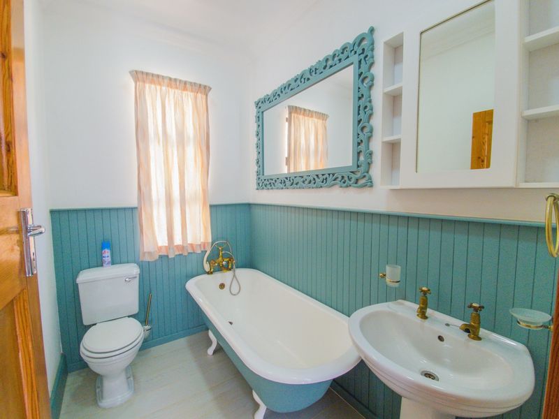 A charming bathroom featuring a classic clawfoot bathtub, pedestal sink, and decorative beadboard wainscoting with vintage-style brass fixtures.