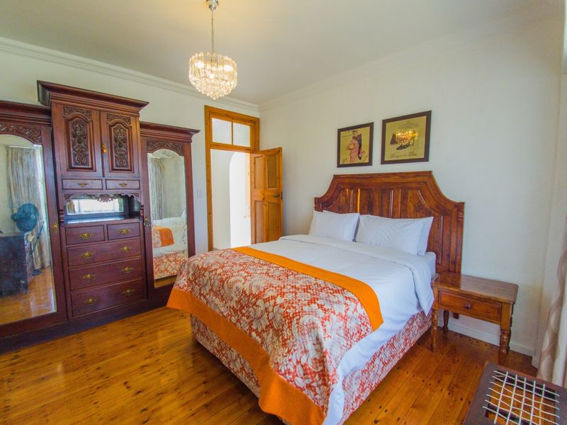 A well-maintained bedroom featuring polished hardwood flooring, crown molding, and a classic crystal chandelier, offering a warm and inviting atmosphere.