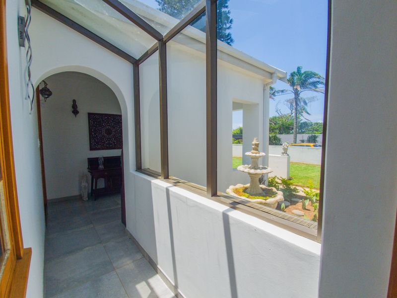 A bright, glass-enclosed patio area featuring tiled flooring, an arched entrance, and a view of the garden with a stone fountain.