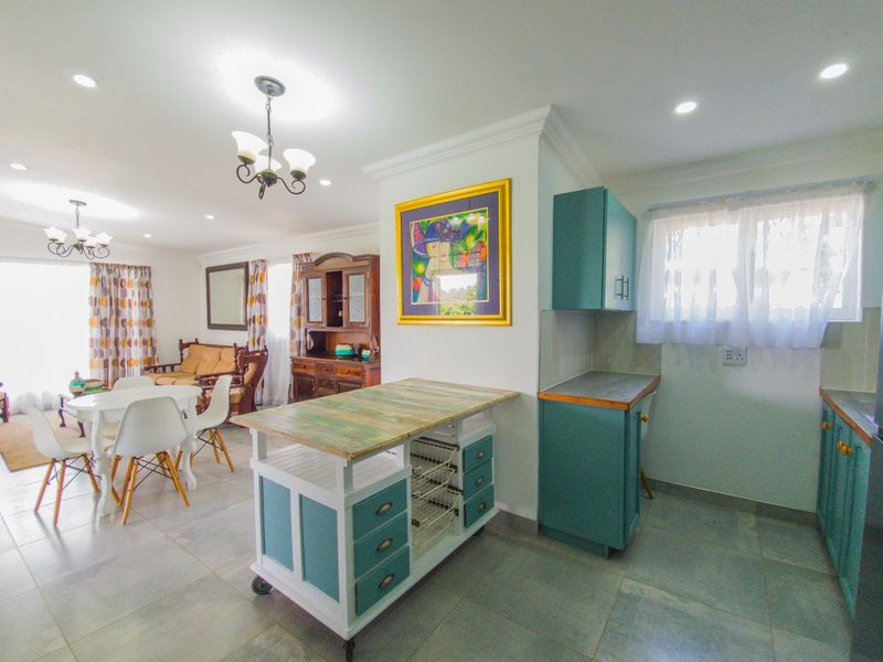 Open-plan living and kitchen area featuring tiled flooring, recessed lighting, and teal-toned kitchen cabinetry with a central mobile island unit.