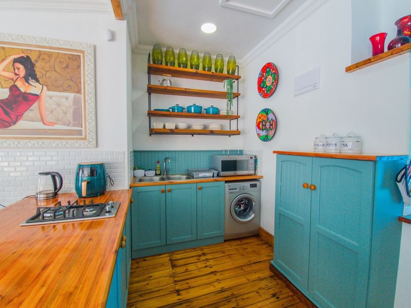 A charming kitchen featuring teal cabinetry, warm timber countertops, subway tile backsplash, and integrated laundry facilities, complemented by natural timber flooring.