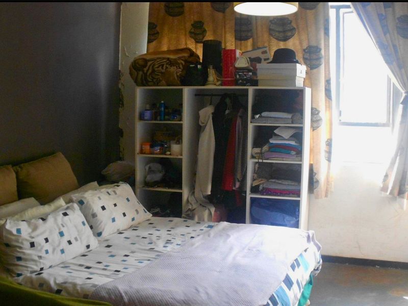 A bedroom featuring a window and basic lighting, currently showing signs of wear including peeling paint on the wall.