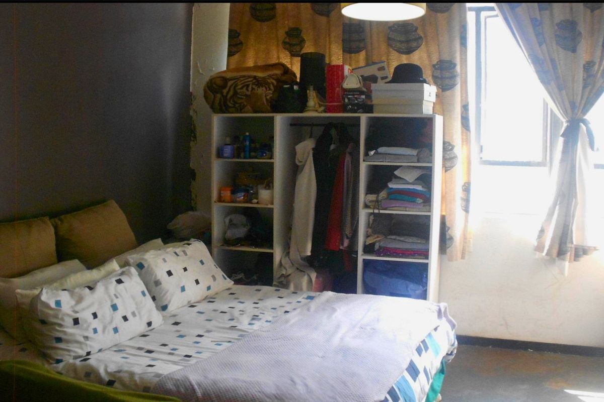 A bedroom featuring a window and basic lighting, currently showing signs of wear including peeling paint on the wall.