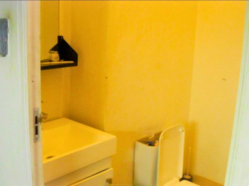 A compact bathroom featuring a wall-mounted basin with vanity storage and a standard toilet, requiring cosmetic updates to improve the overall aesthetic.