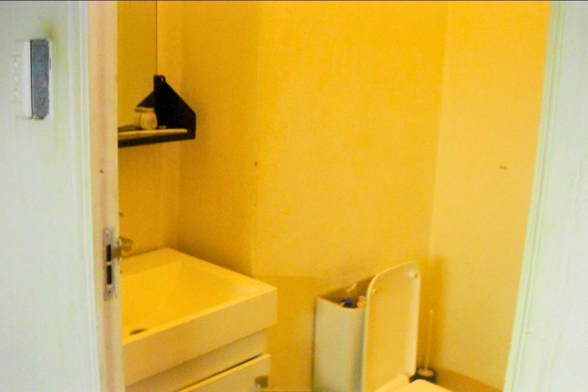 A compact bathroom featuring a wall-mounted basin with vanity storage and a standard toilet, requiring cosmetic updates to improve the overall aesthetic.