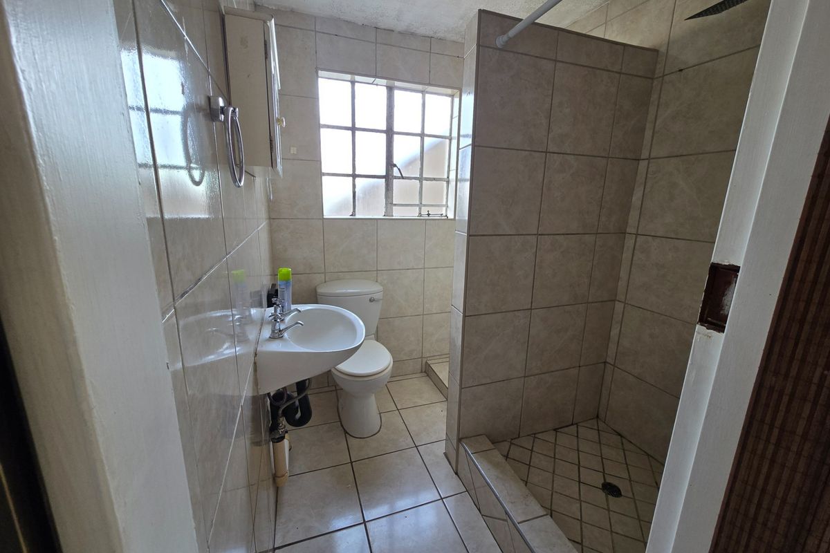 A functional bathroom featuring a walk-in shower, wall-mounted basin, and toilet, finished with neutral wall and floor tiles.