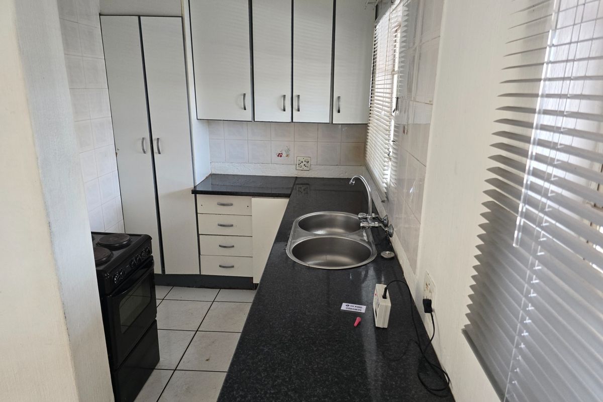 A functional kitchen featuring dark granite countertops, white built-in cabinetry, a double bowl sink, and tiled flooring with a neutral backsplash.