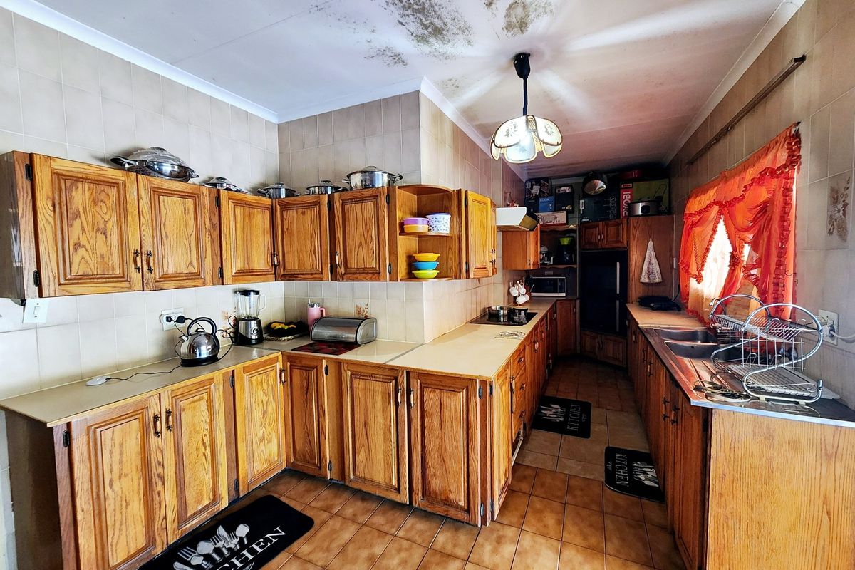 A dated kitchen featuring wooden cabinetry, laminate countertops, and a double bowl sink, requiring ceiling repairs due to visible water damage.