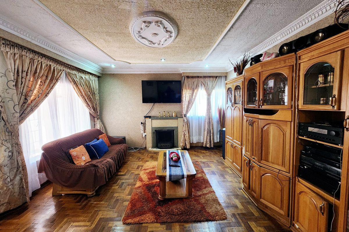 A traditional living room featuring parquet flooring, a central fireplace, and decorative ceiling detailing, offering a classic layout with potential for modern updates.