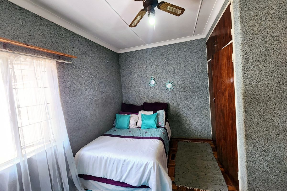 A compact bedroom featuring parquet flooring, a ceiling fan, and built-in wooden wardrobes with a textured wall finish.