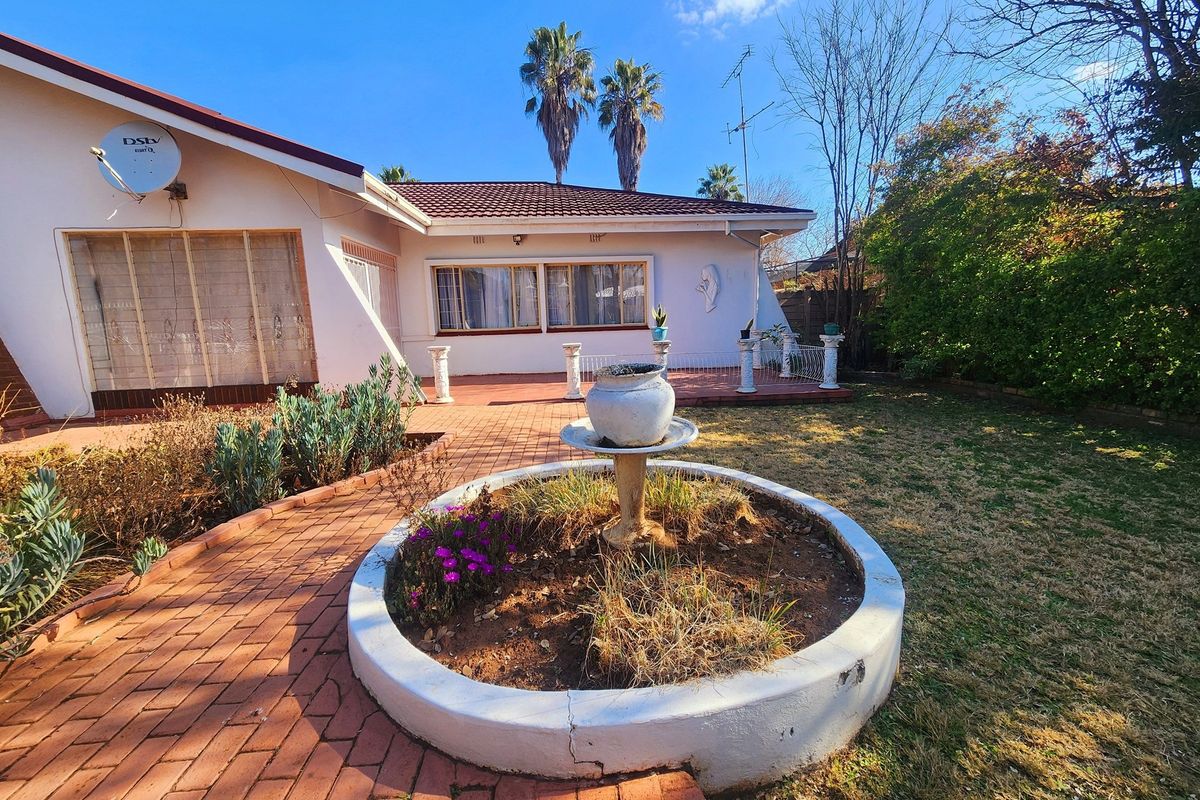 Rear exterior view of the house featuring a brick-paved patio, a central concrete fountain, and a landscaped garden area.