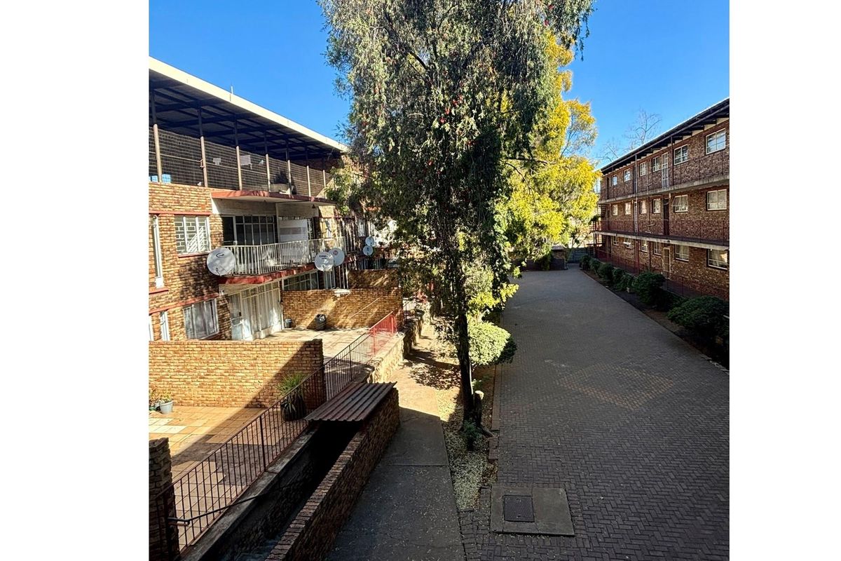 Exterior view of the apartment complex featuring brick facade buildings, paved driveway, and private ground-floor patio areas.