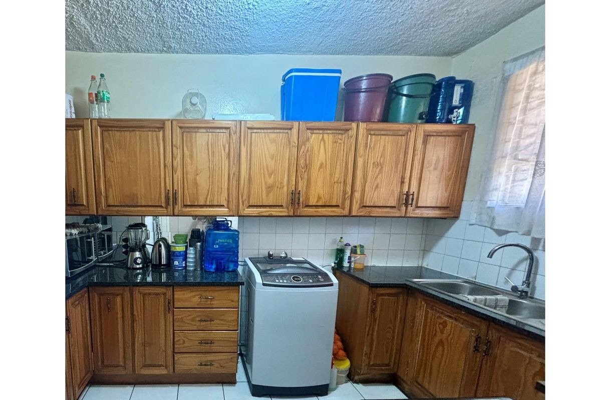 A functional kitchen featuring wood-toned cabinetry, granite countertops, a stainless steel sink, and a dedicated space for a top-loading washing machine.