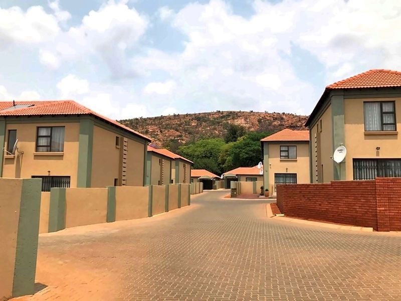 A view of a residential complex street featuring paved driveways, boundary walls, and multiple double-story houses with tiled roofs.