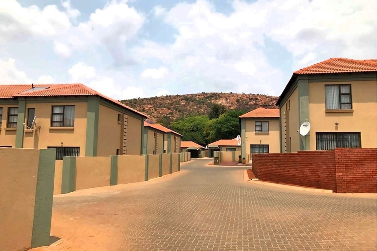 A view of a residential complex street featuring paved driveways, boundary walls, and multiple double-story houses with tiled roofs.