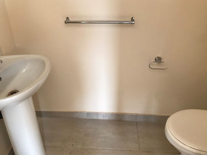 A functional bathroom featuring a pedestal basin, toilet, and chrome fixtures, finished with tiled flooring.