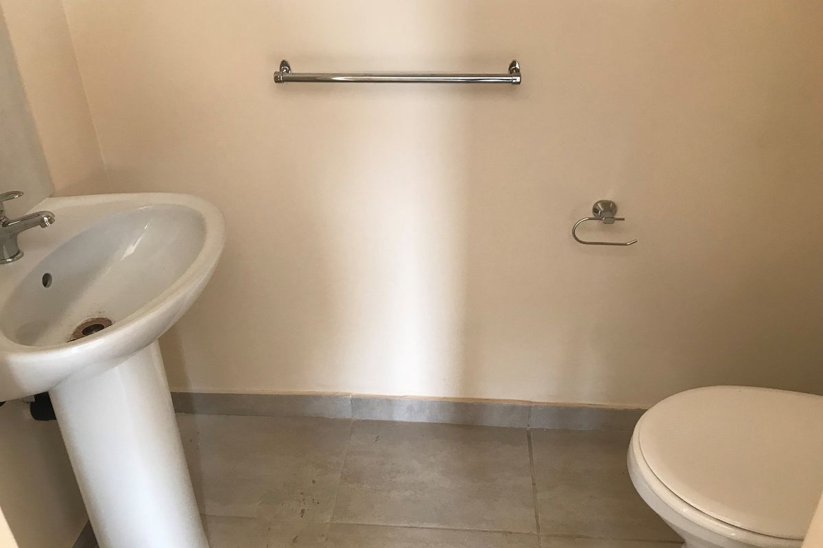 A functional bathroom featuring a pedestal basin, toilet, and chrome fixtures, finished with tiled flooring.