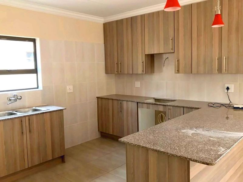 A functional kitchen featuring wood-look laminate cabinetry, granite countertops, a double bowl sink, and tiled backsplash, currently awaiting appliance installation.