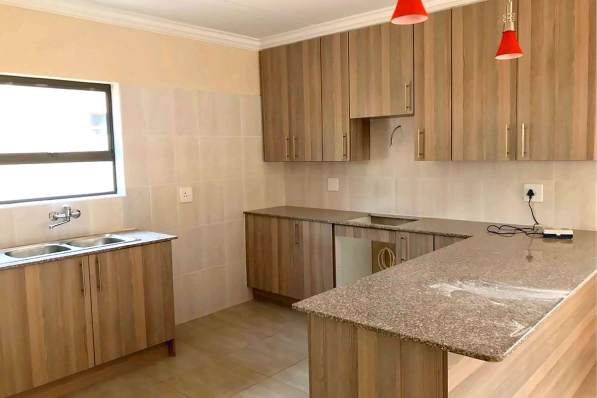 A functional kitchen featuring wood-look laminate cabinetry, granite countertops, a double bowl sink, and tiled backsplash, currently awaiting appliance installation.