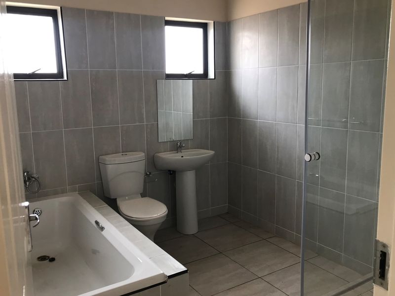 A clean, modern bathroom featuring a bathtub, separate glass shower enclosure, pedestal basin, and neutral grey wall and floor tiling.