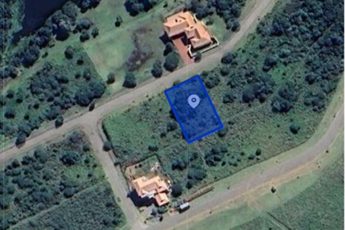 An aerial view of a vacant residential plot highlighted in blue, situated within a developed estate with surrounding greenery and access roads.