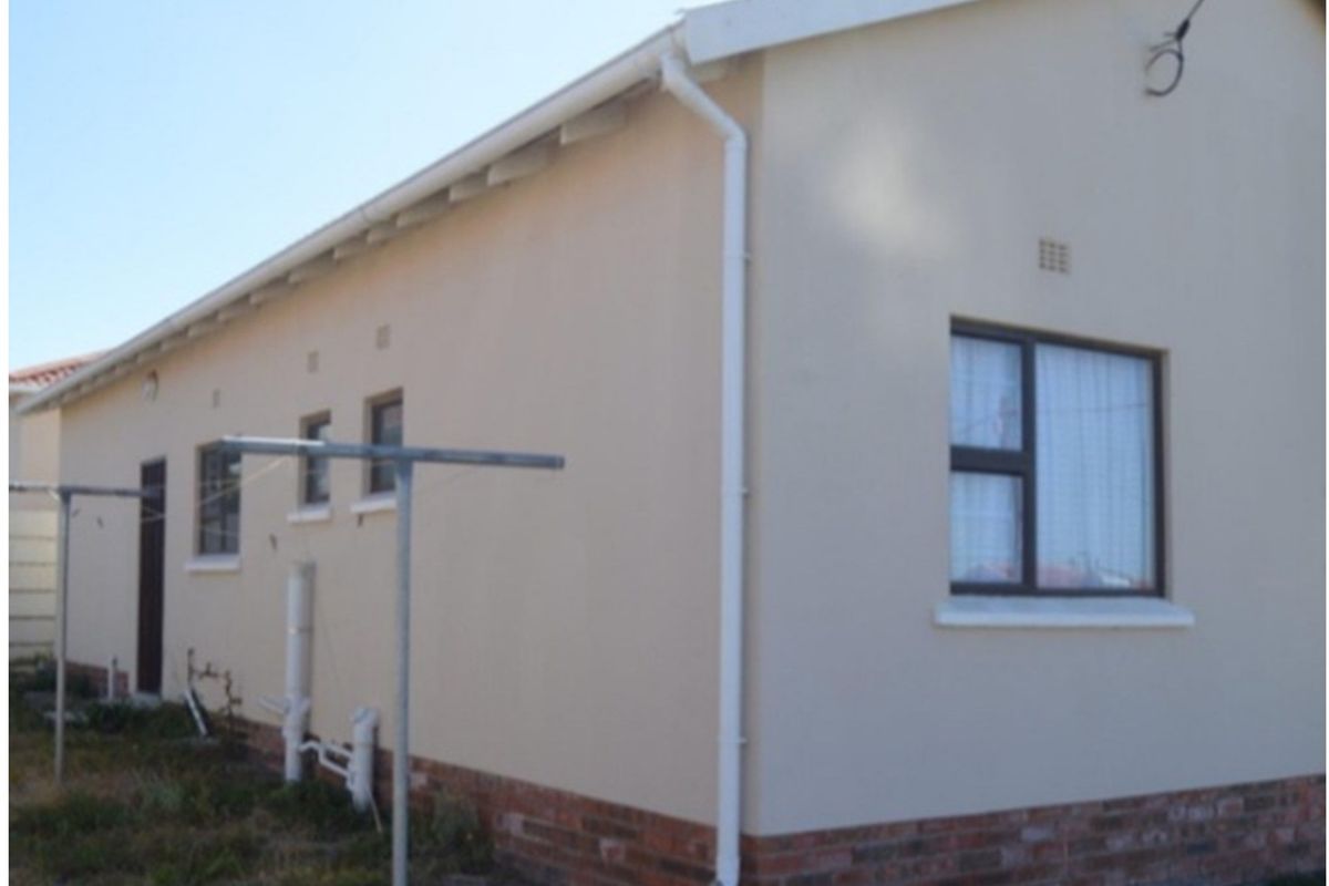 A view of the side exterior elevation of the house, featuring a plastered finish, brick base, and white guttering system.