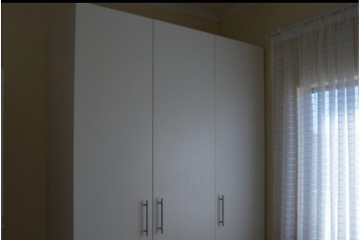 A bedroom featuring built-in white cabinetry with modern handles and a window dressed with sheer curtains.