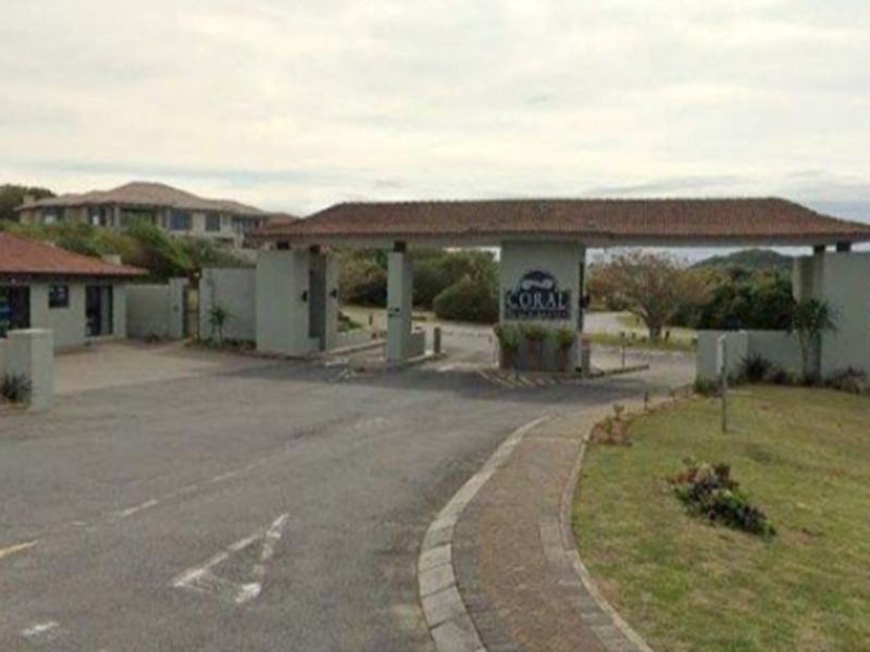 The main entrance gate and security access point for the Coral residential estate, featuring a paved driveway and established landscaping.