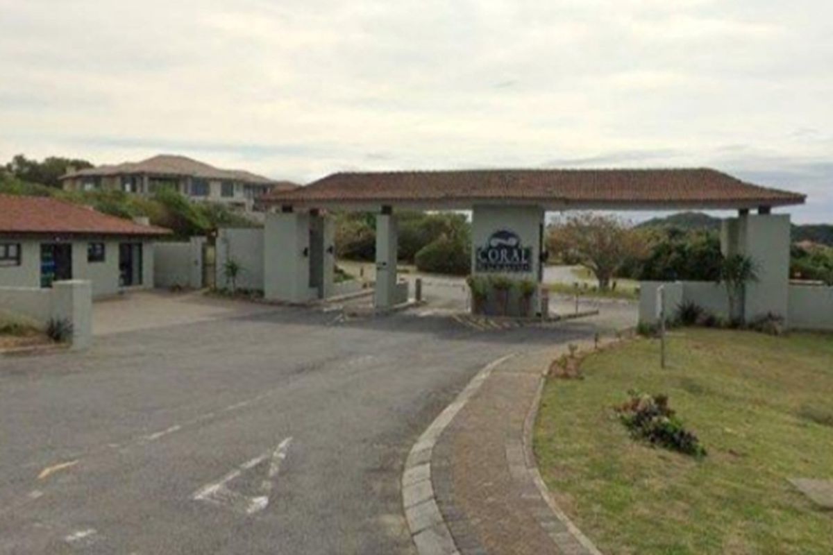 The main entrance gate and security access point for the Coral residential estate, featuring a paved driveway and established landscaping.